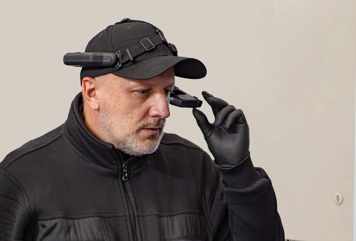 Person mit einem an der Kappe befestigten Kopfdisplay, die dessen Position vor dem Auge einstellt.